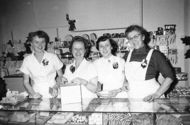 An old image of four woman working behind the counter at the bakery. The wives of the original four brothers