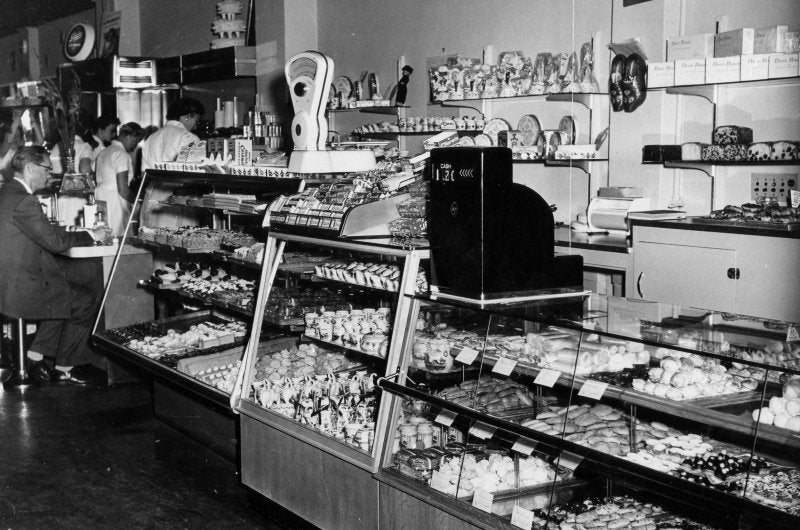 A vintage black and white photo of the display case and cash register of the original coffee shop and bakery